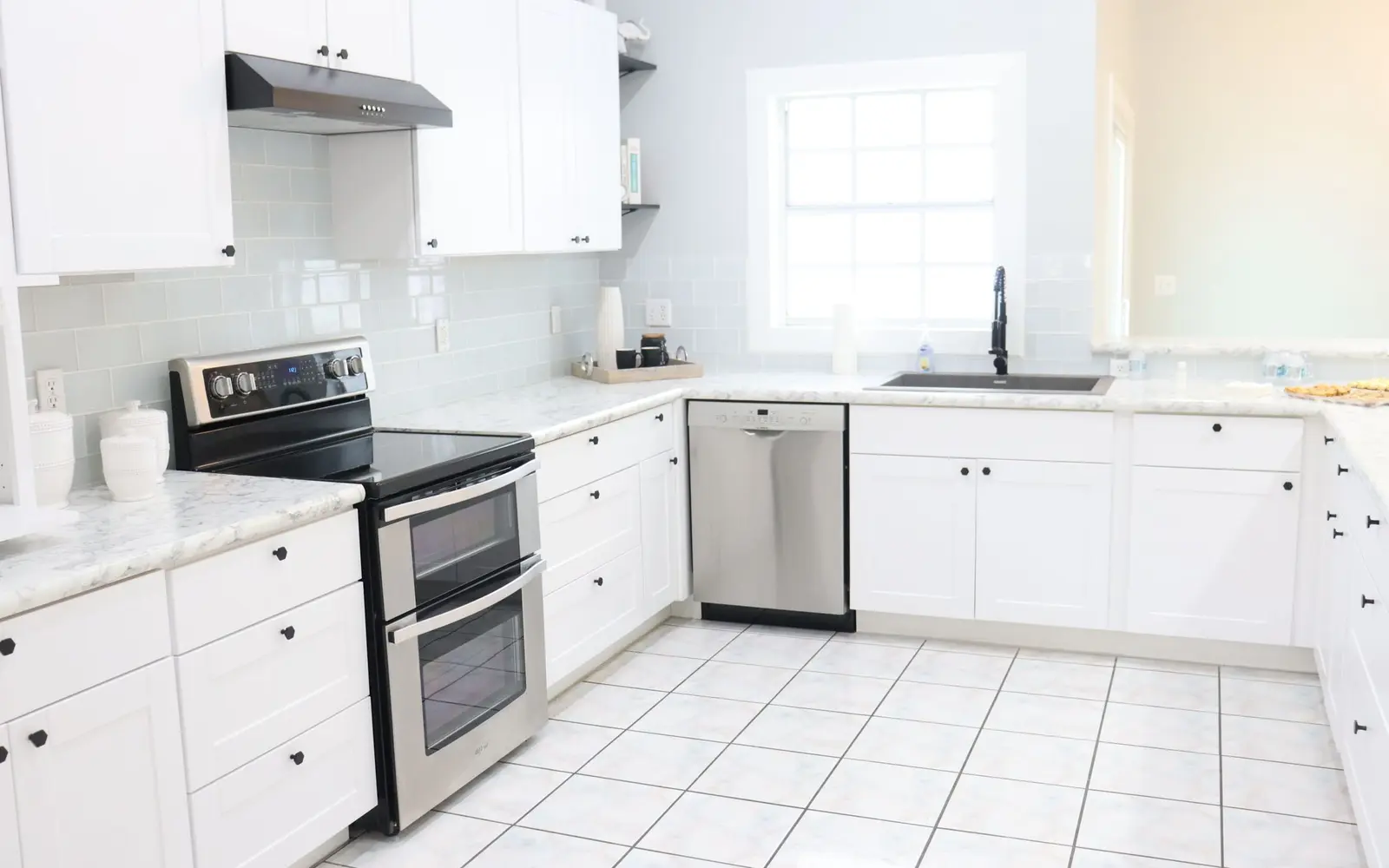 Bright white kitchen with clean counters, stainless appliances and tile floor